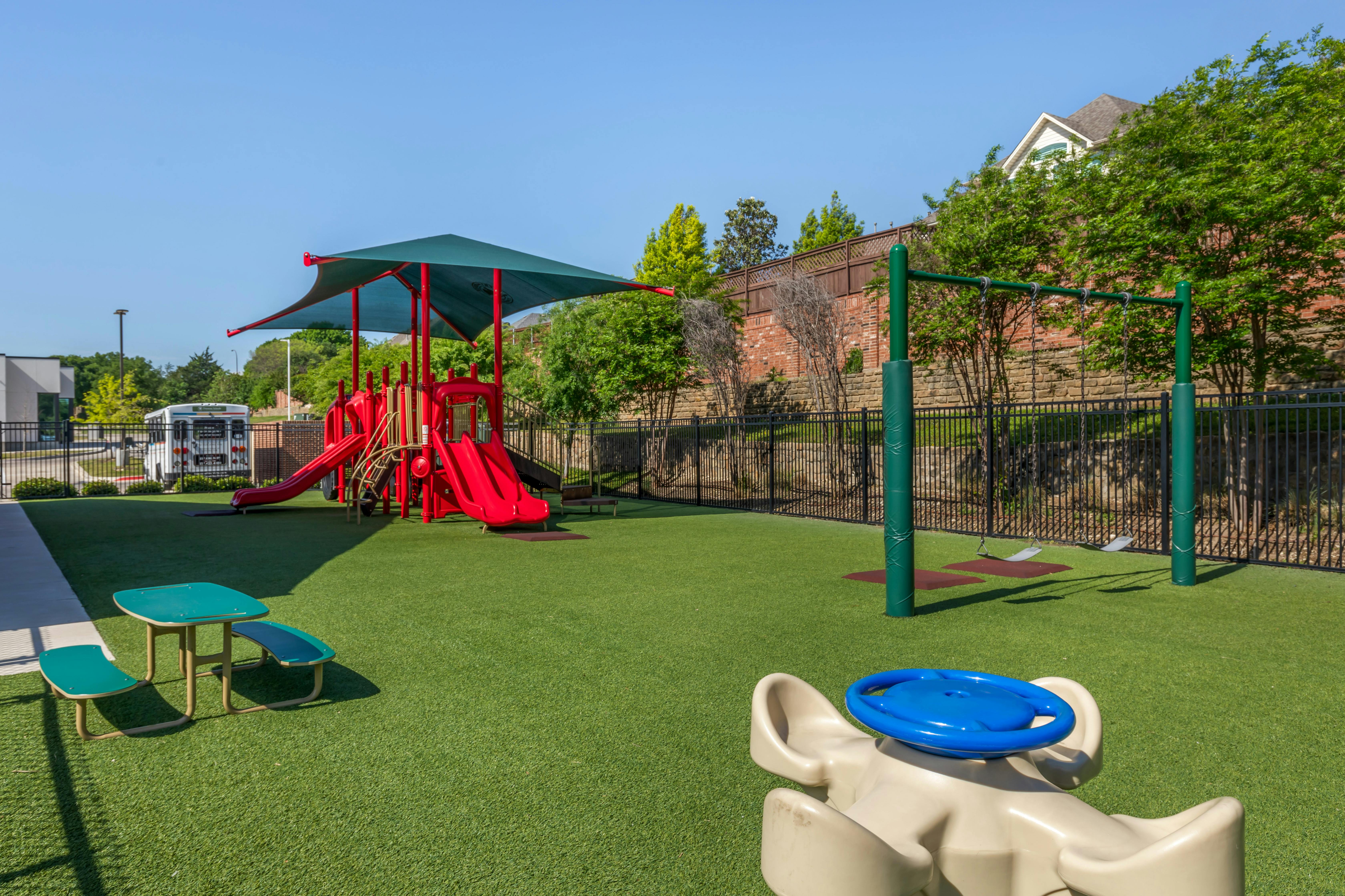 A playground with artificial turf, a red play structure, and swings