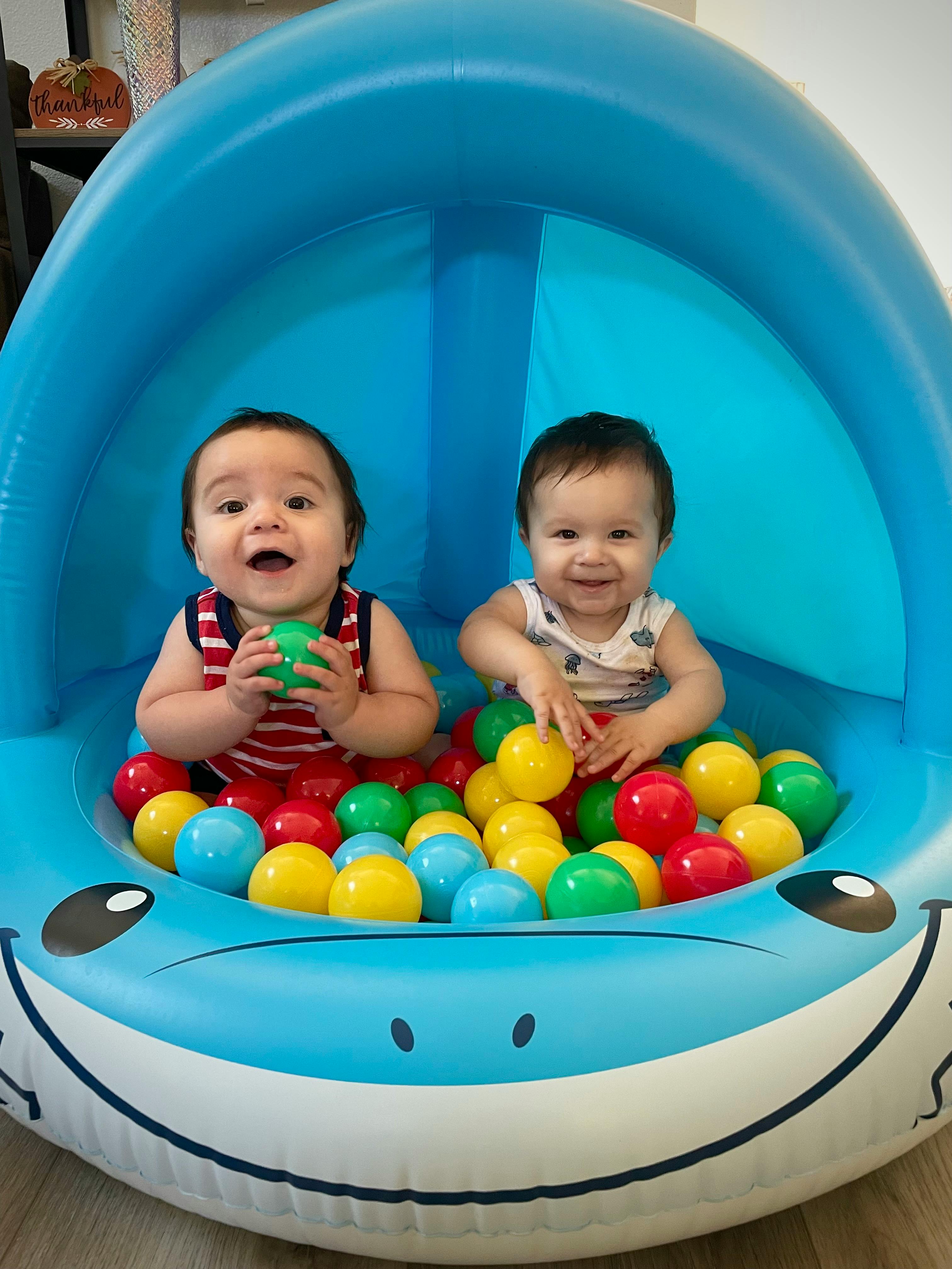 Two children playing in a blue inflatable ball pit with colorful balls