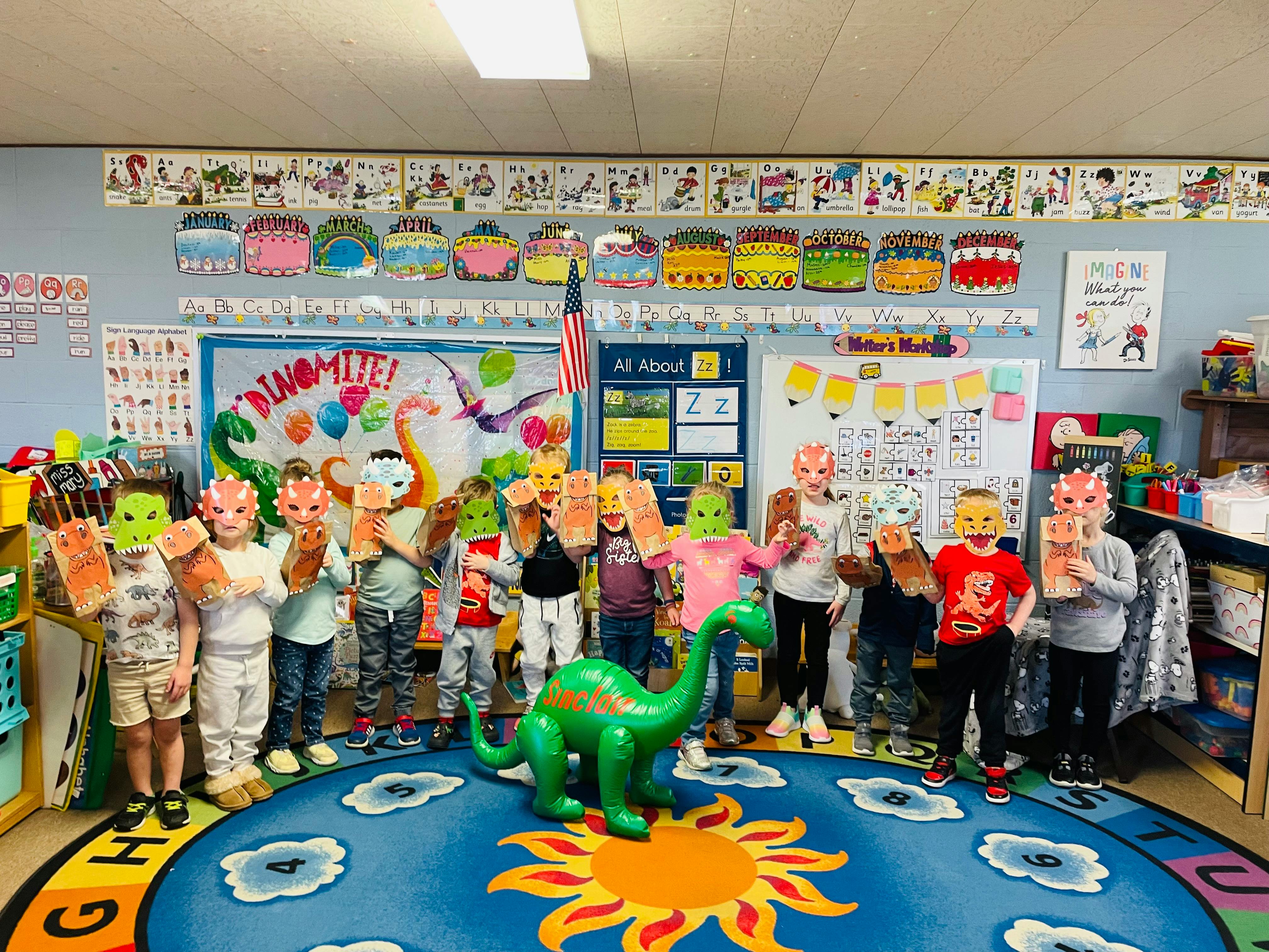 Children in a classroom wearing dinosaur masks and holding up paper cutouts