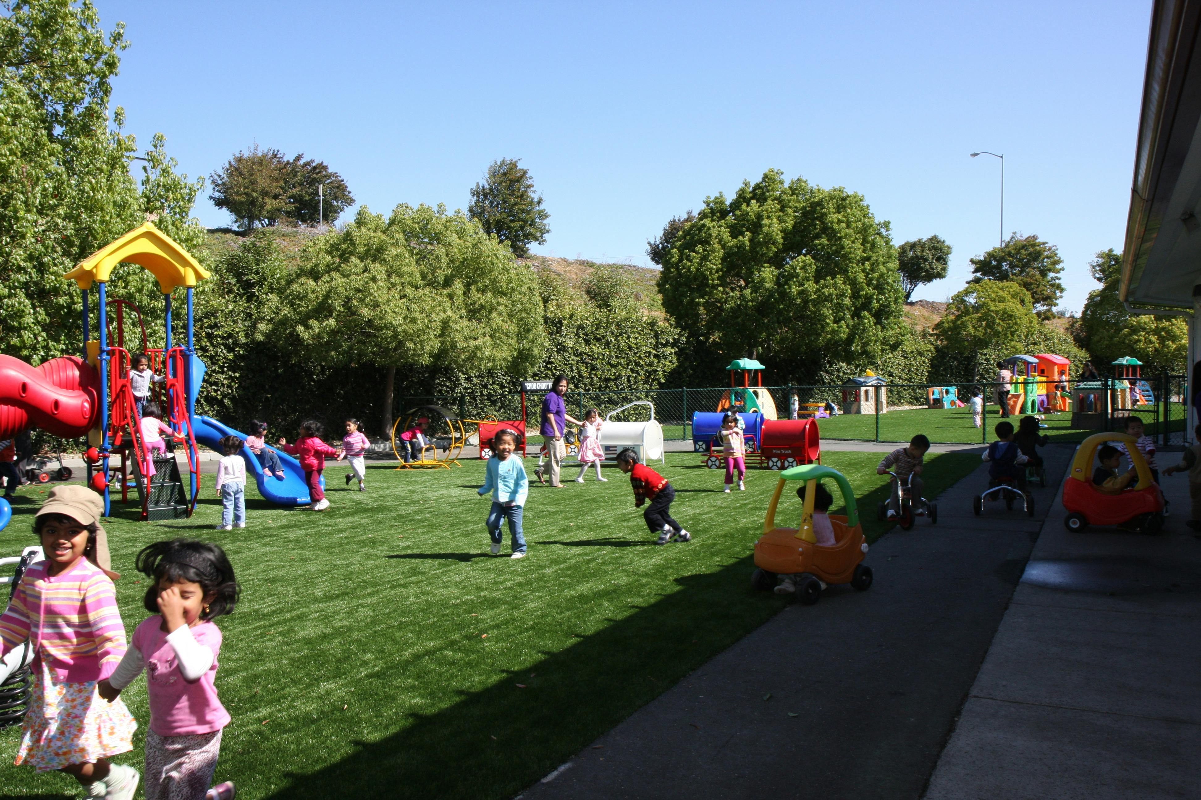 Children playing on a grassy playground with play structures
