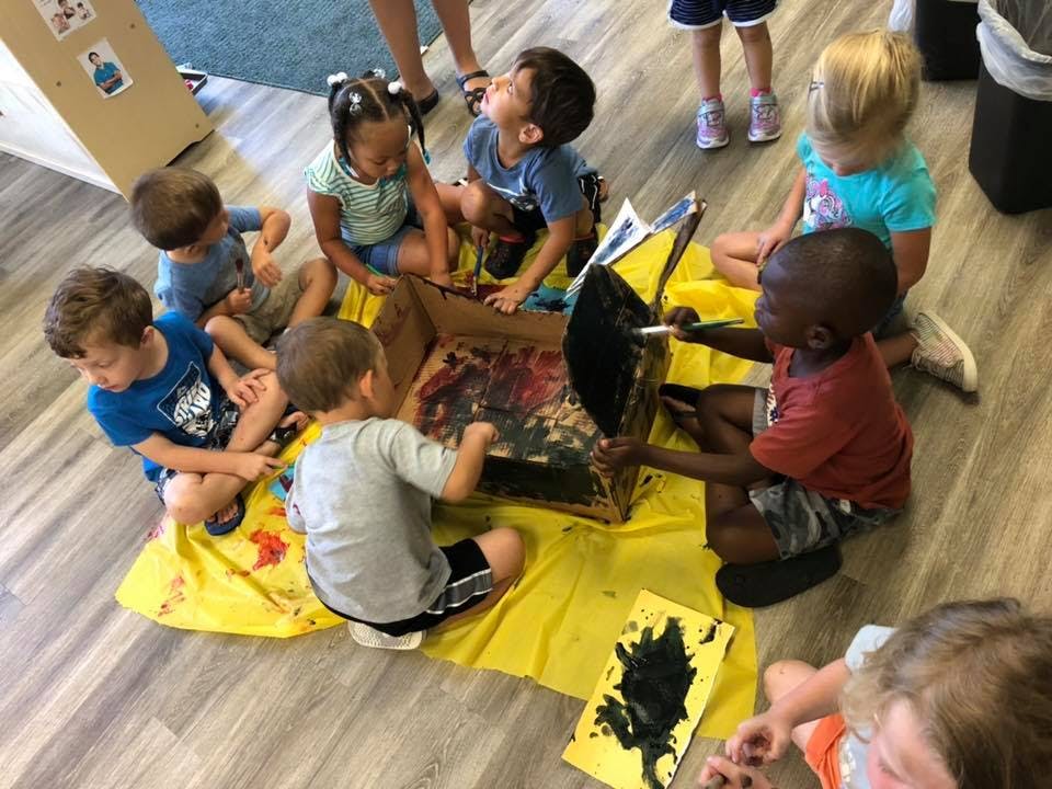 Children sitting on the floor around a box, looking inside