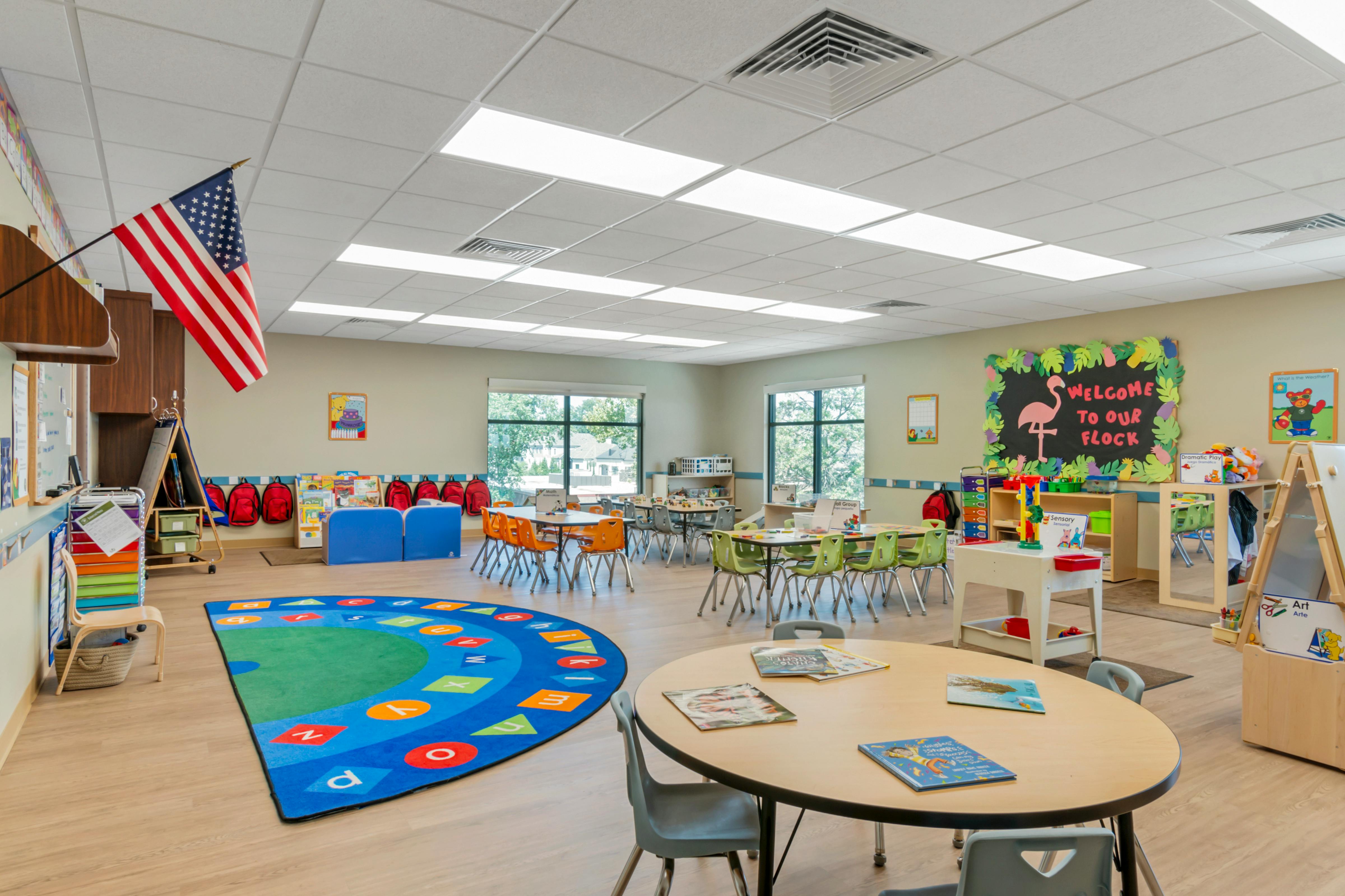 Classroom with tables, chairs, colorful rug, and a "Welcome to Our Flock" sign