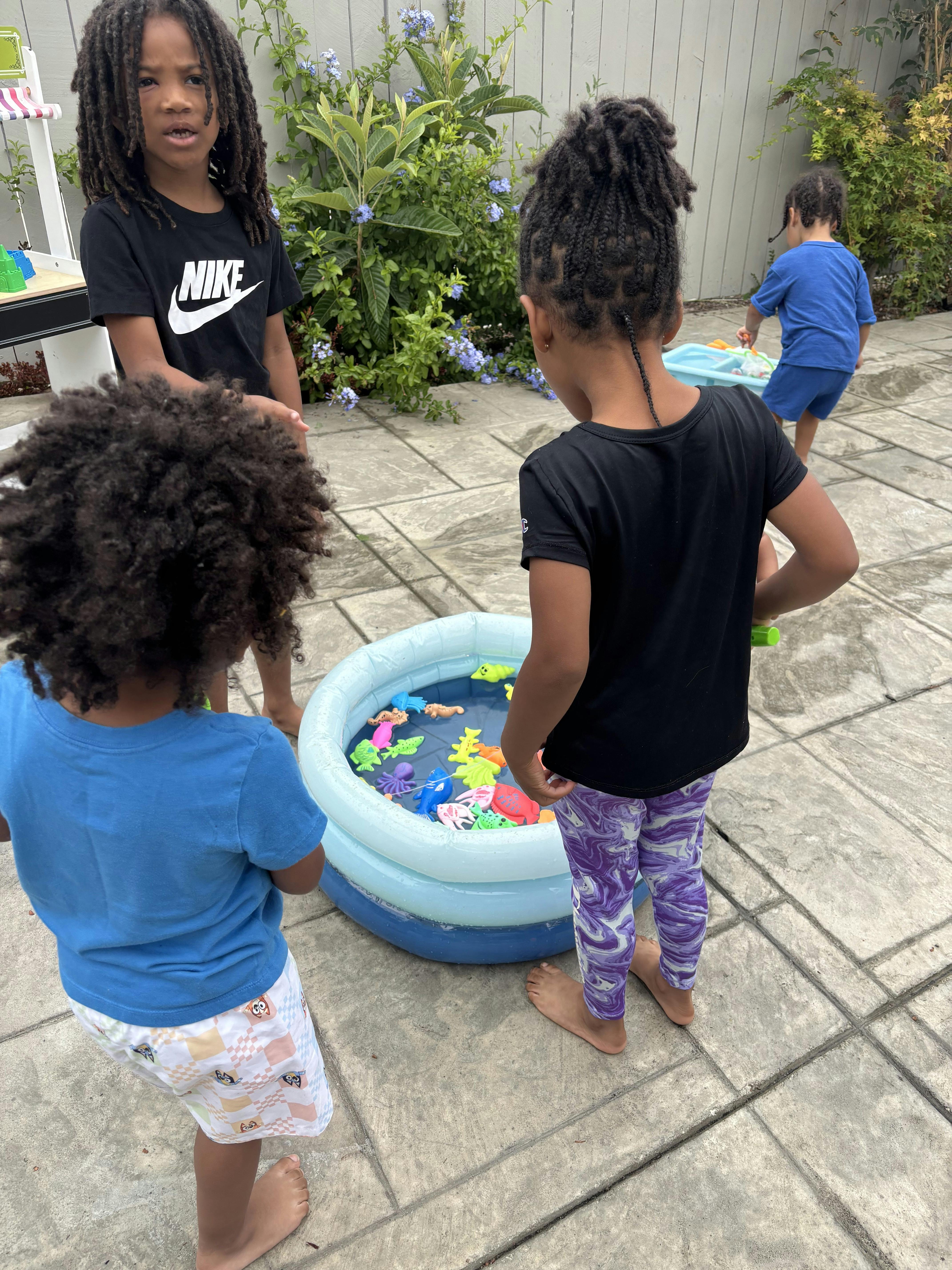 Three children playing around a small inflatable pool with toys