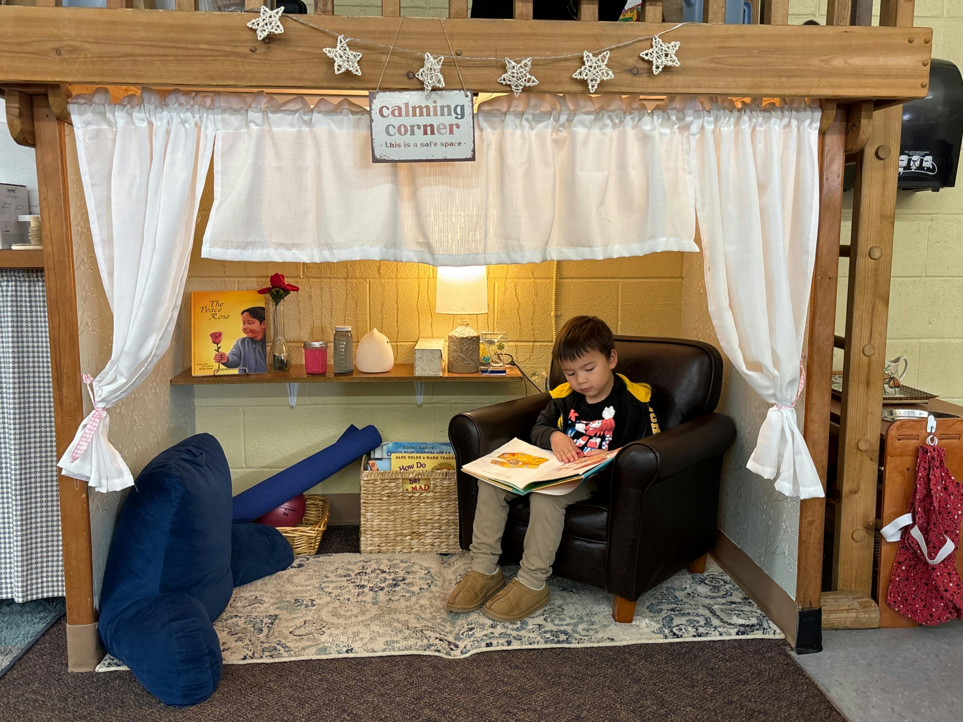 Child sitting in a chair reading a book in a calming corner