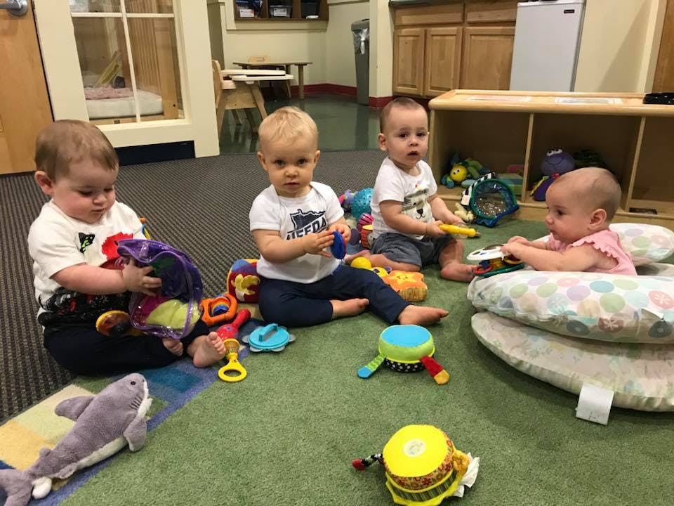 Four babies playing with toys on a green carpet