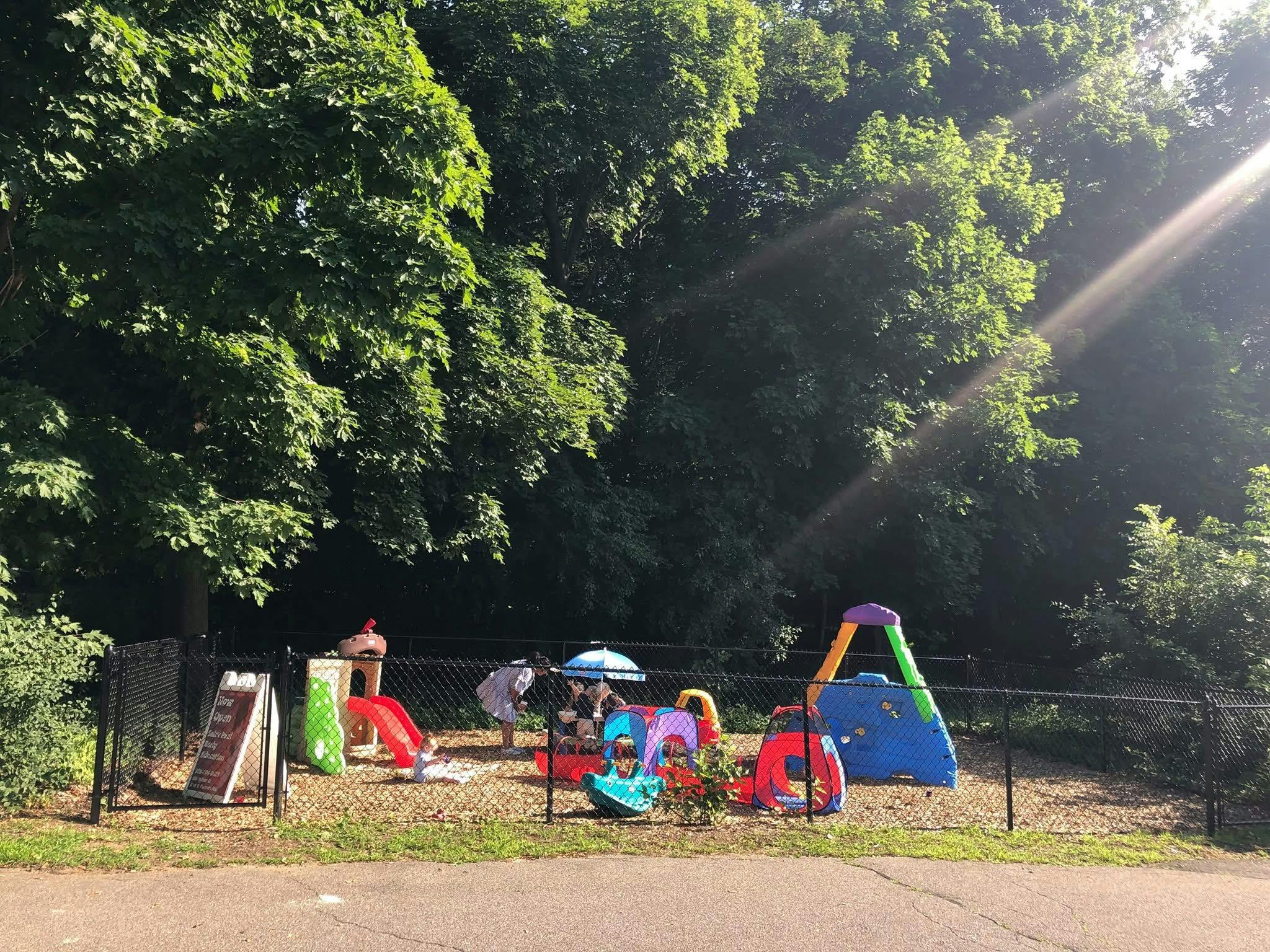 People and children playing in a fenced-in playground with colorful equipment