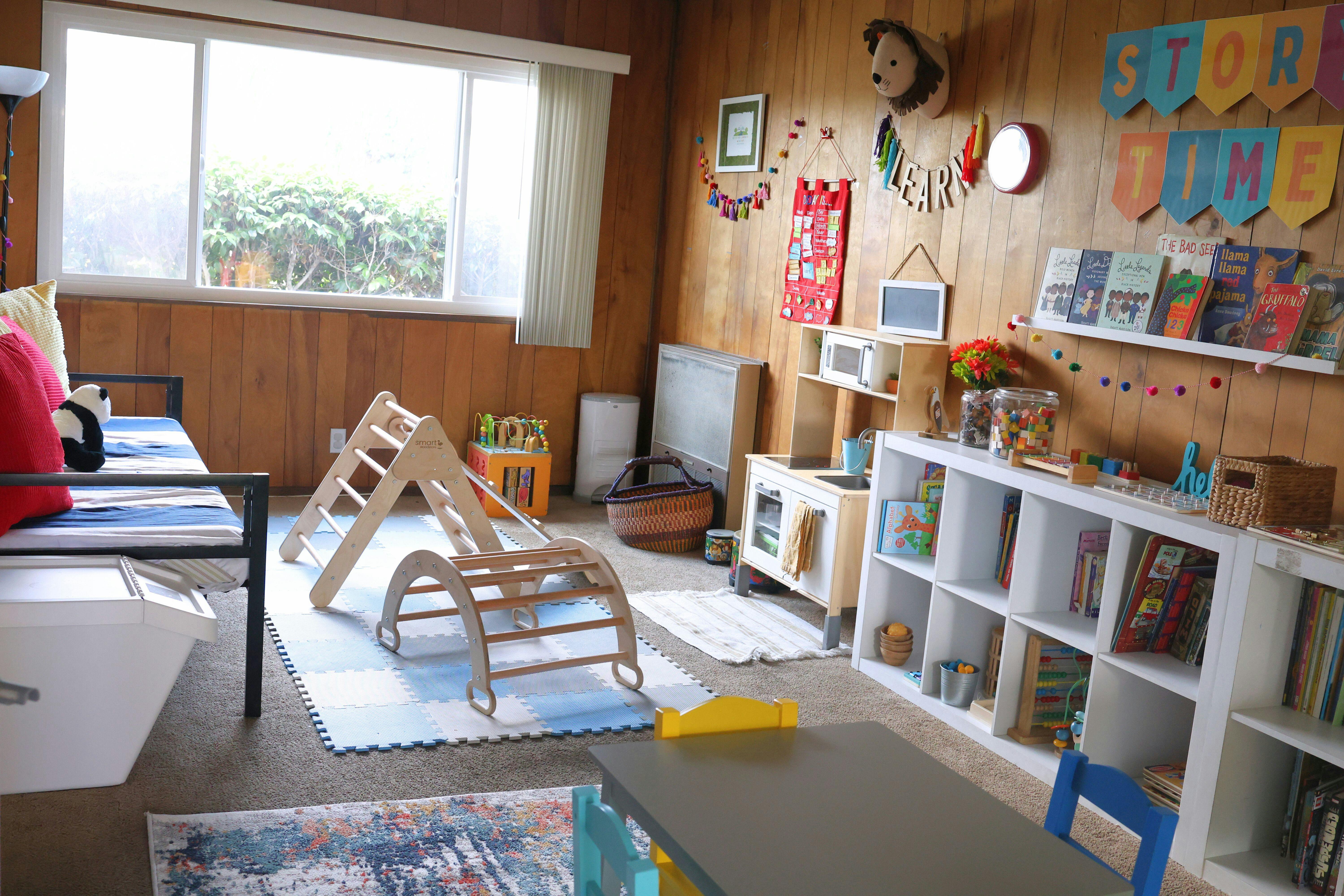 Indoor play area with wooden climbing structures, shelves of books, and a window