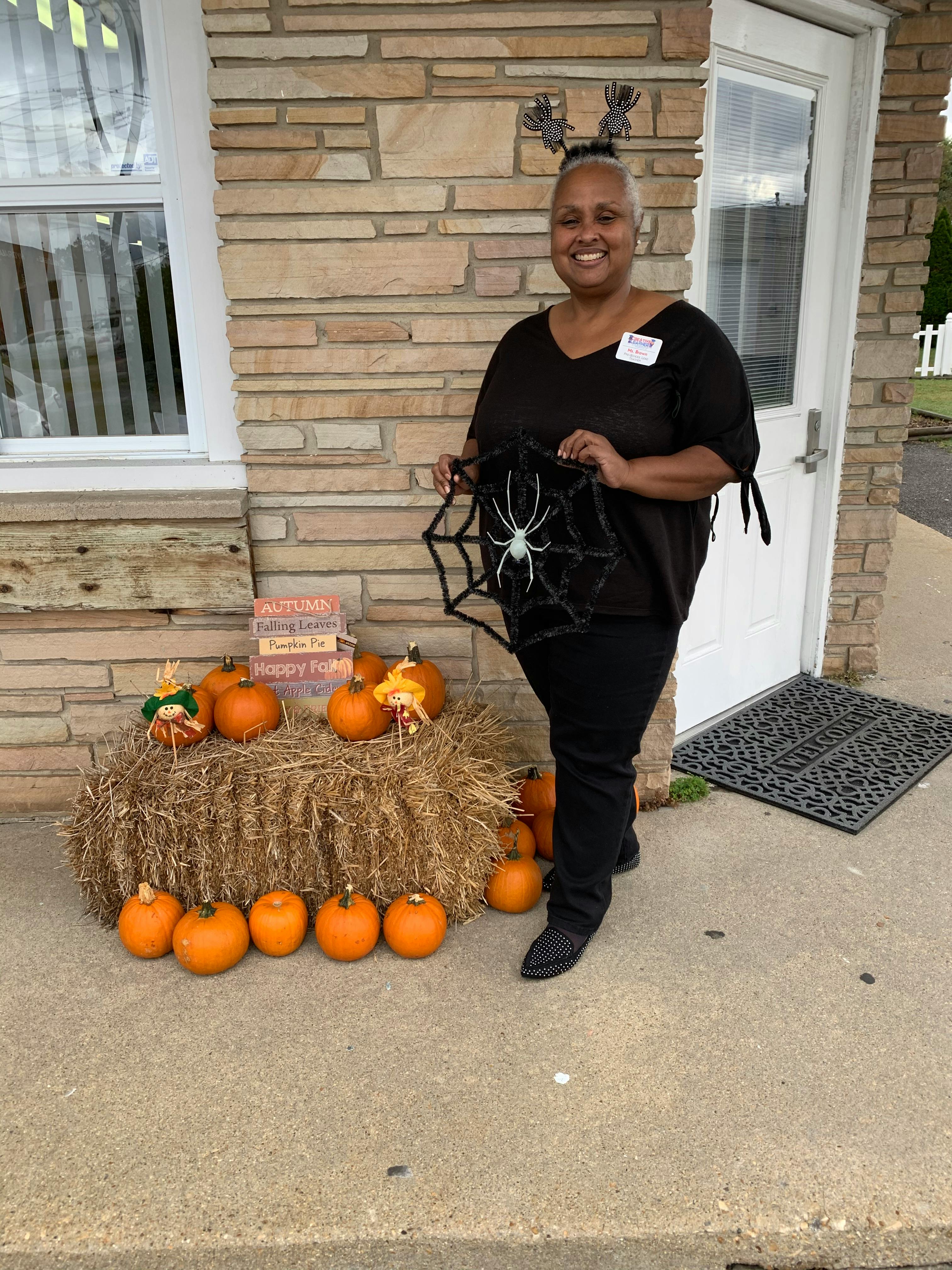 Person holding a spiderweb decoration next to a hay bale and pumpkins