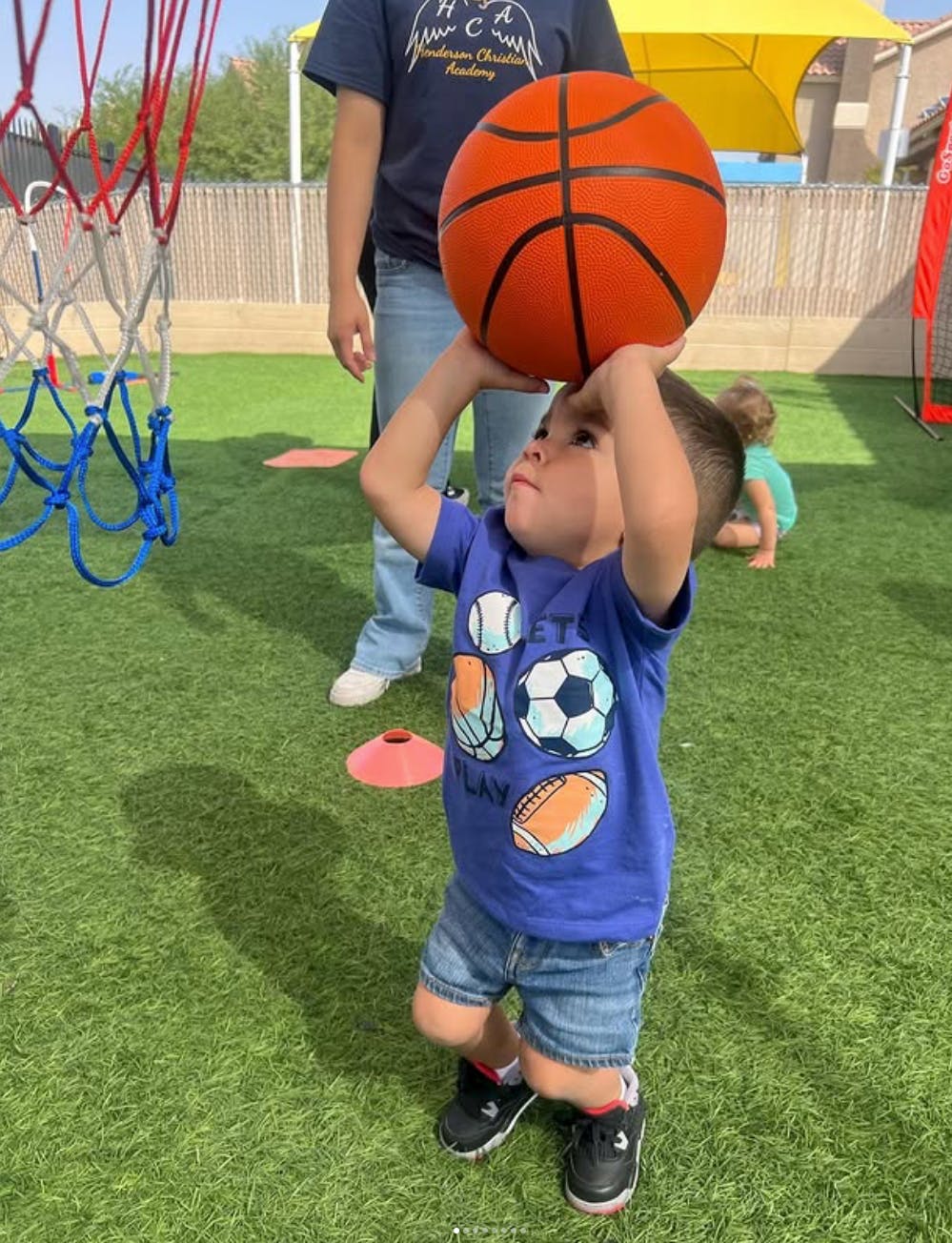 Child in a blue shirt holding a basketball overhead on a green turf