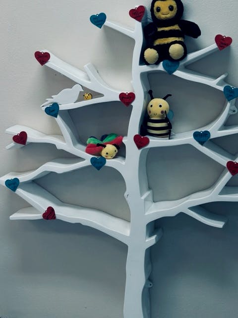 White tree-shaped shelf with bee and ladybug plush toys and heart decorations
