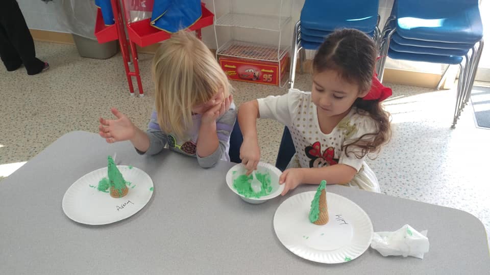 Two children at a table making crafts with green material