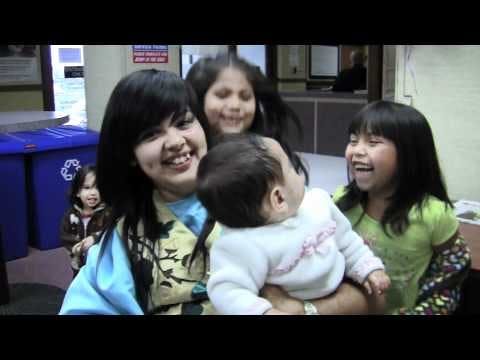 Person holding a baby, with two children smiling nearby