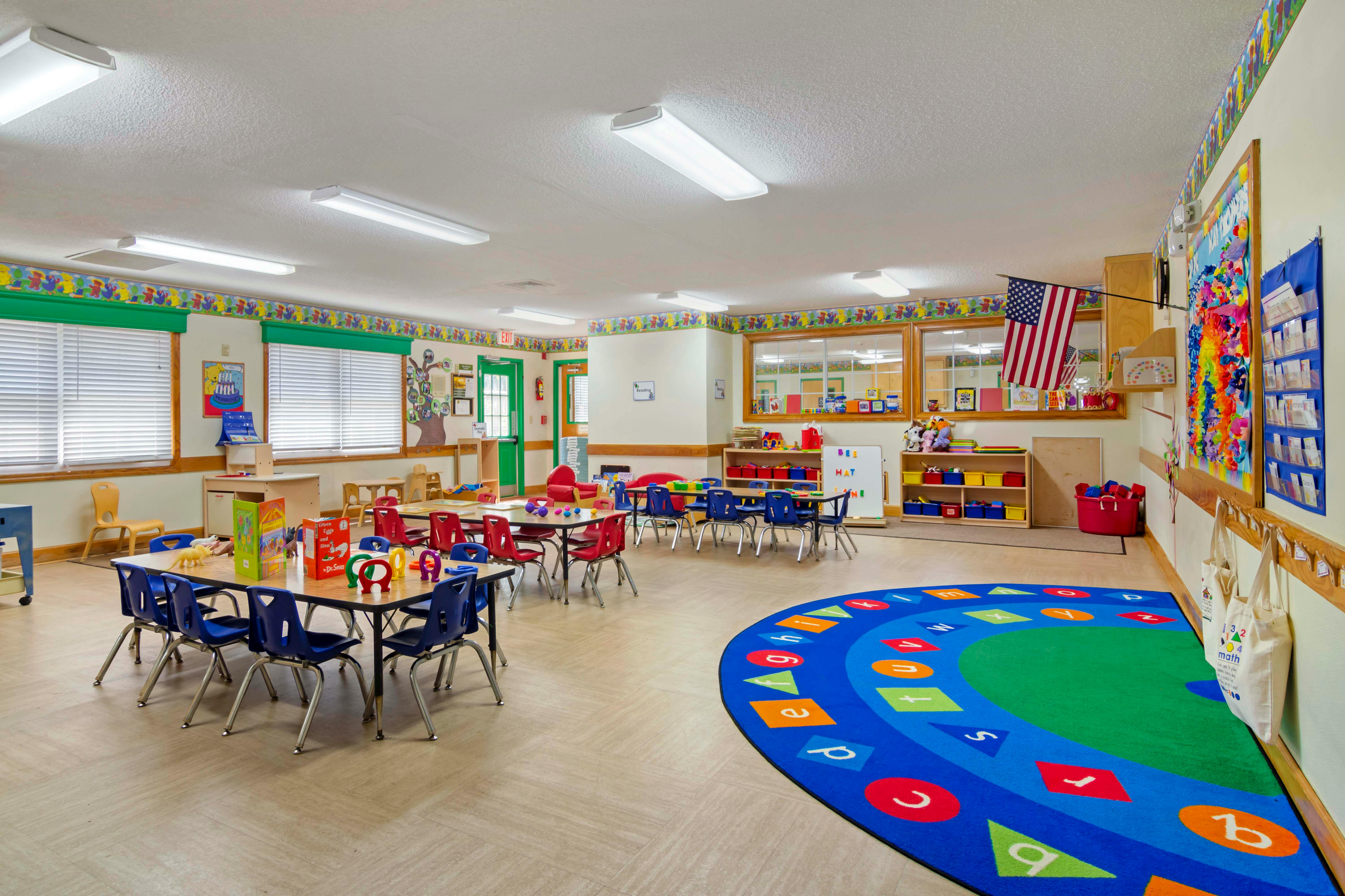 An empty kindergarten classroom with small tables and chairs and a colorful alphabet rug