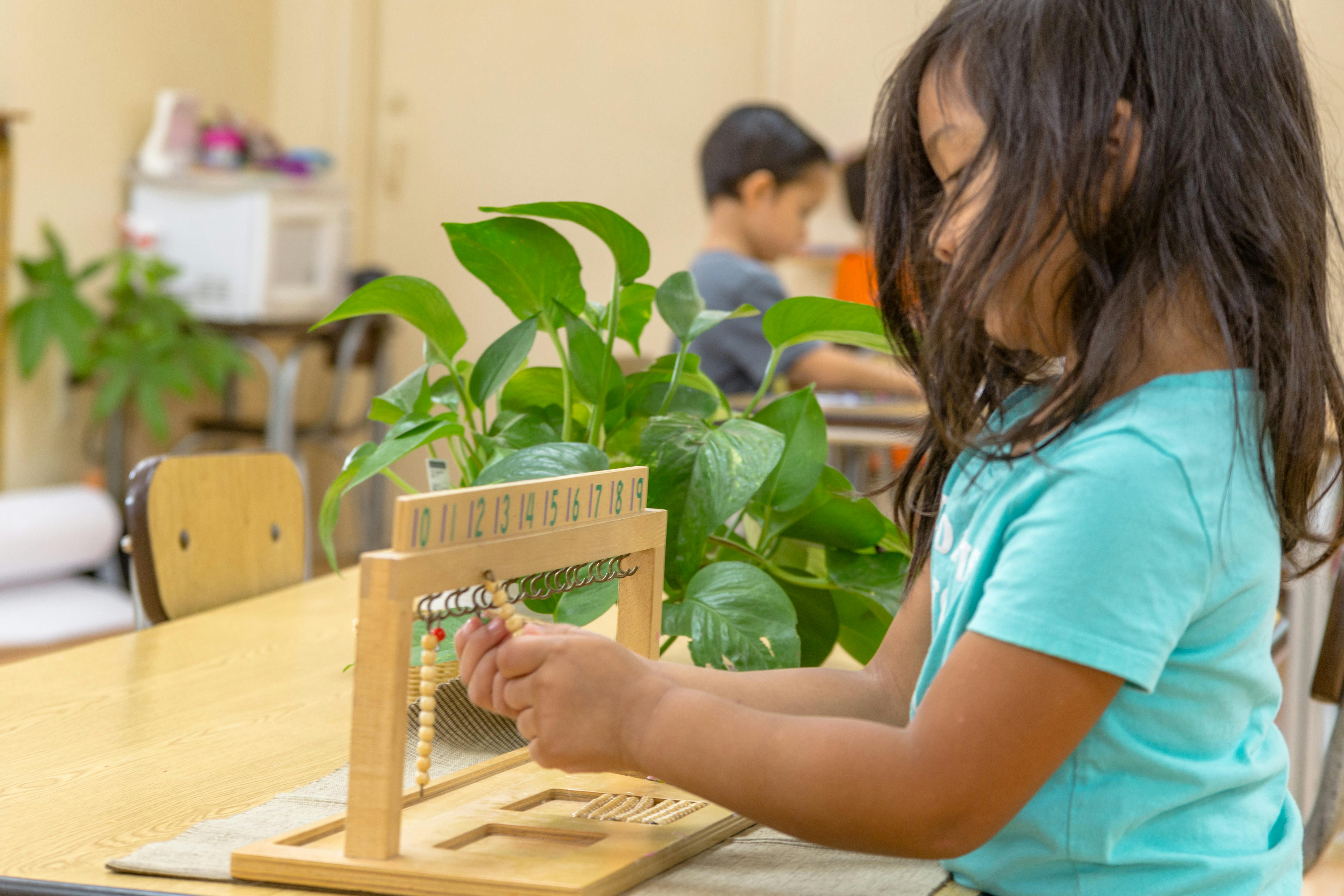 Child manipulating beads on an abacus-like learning tool in a classroom