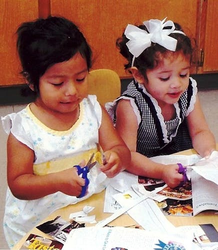 Two children cutting paper with scissors at a table
