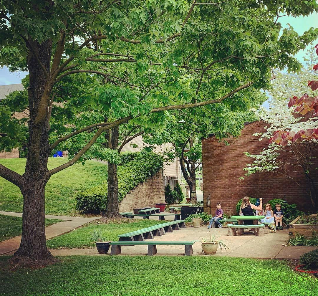 People and children sitting at picnic tables under trees
