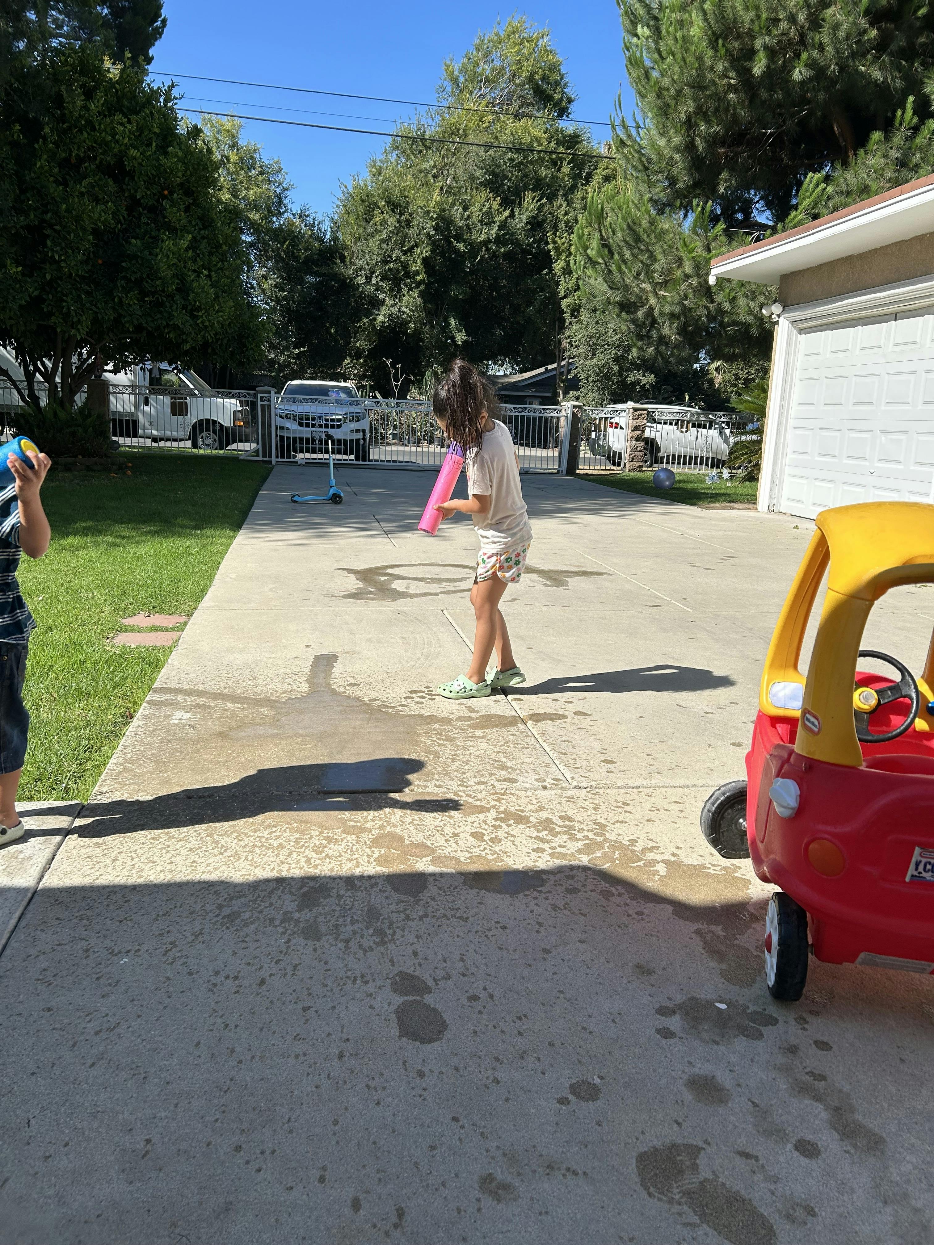 Child playing with a pink toy in a driveway