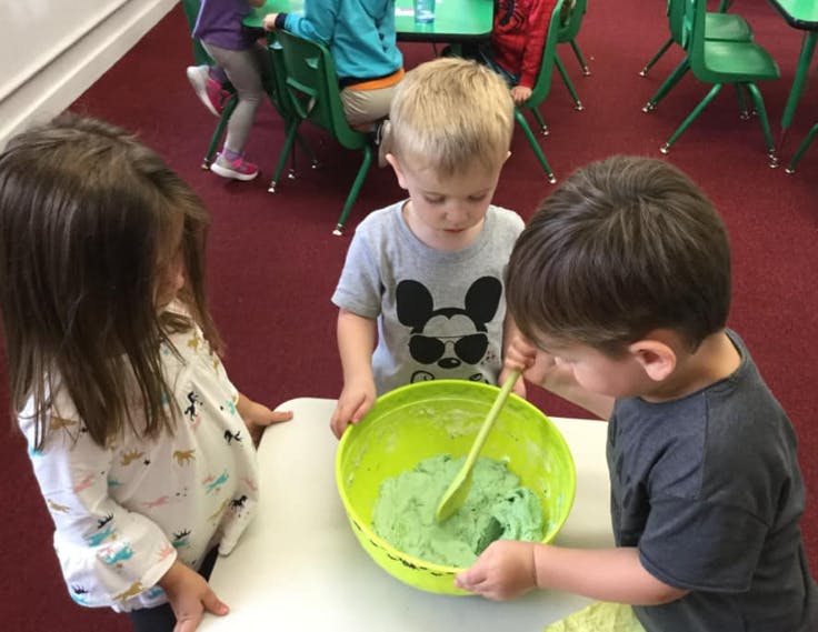 Three children mixing green slime in a bowl