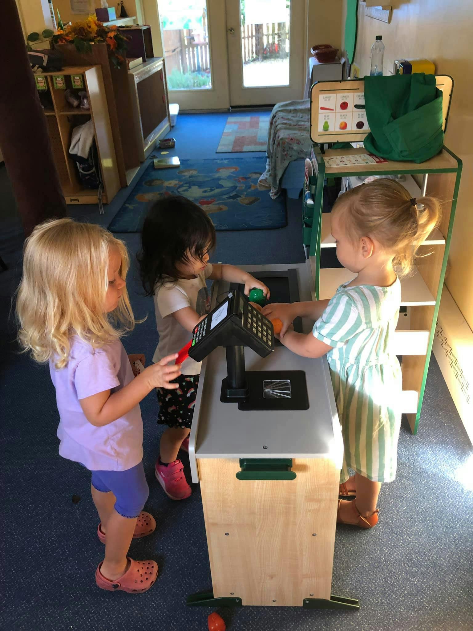Three children playing with a toy cash register in a classroom