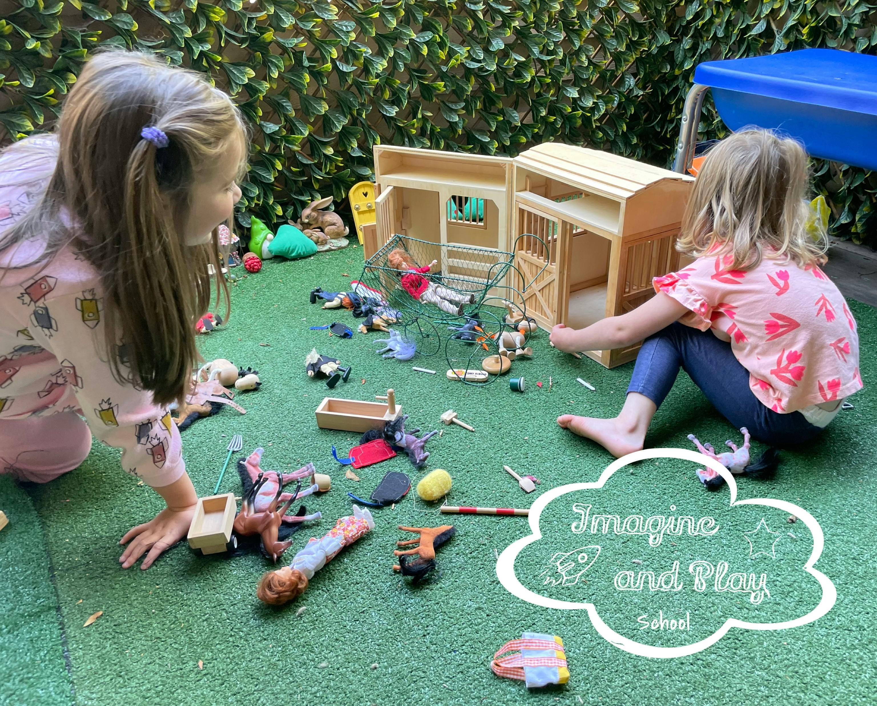 Two children playing with a dollhouse and animal figurines on green turf