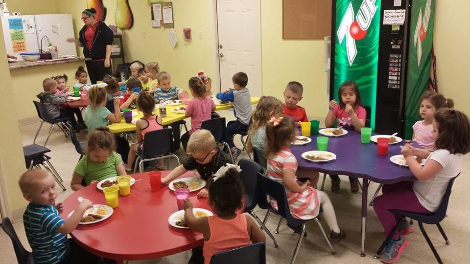 Children sitting at tables eating meals in a classroom