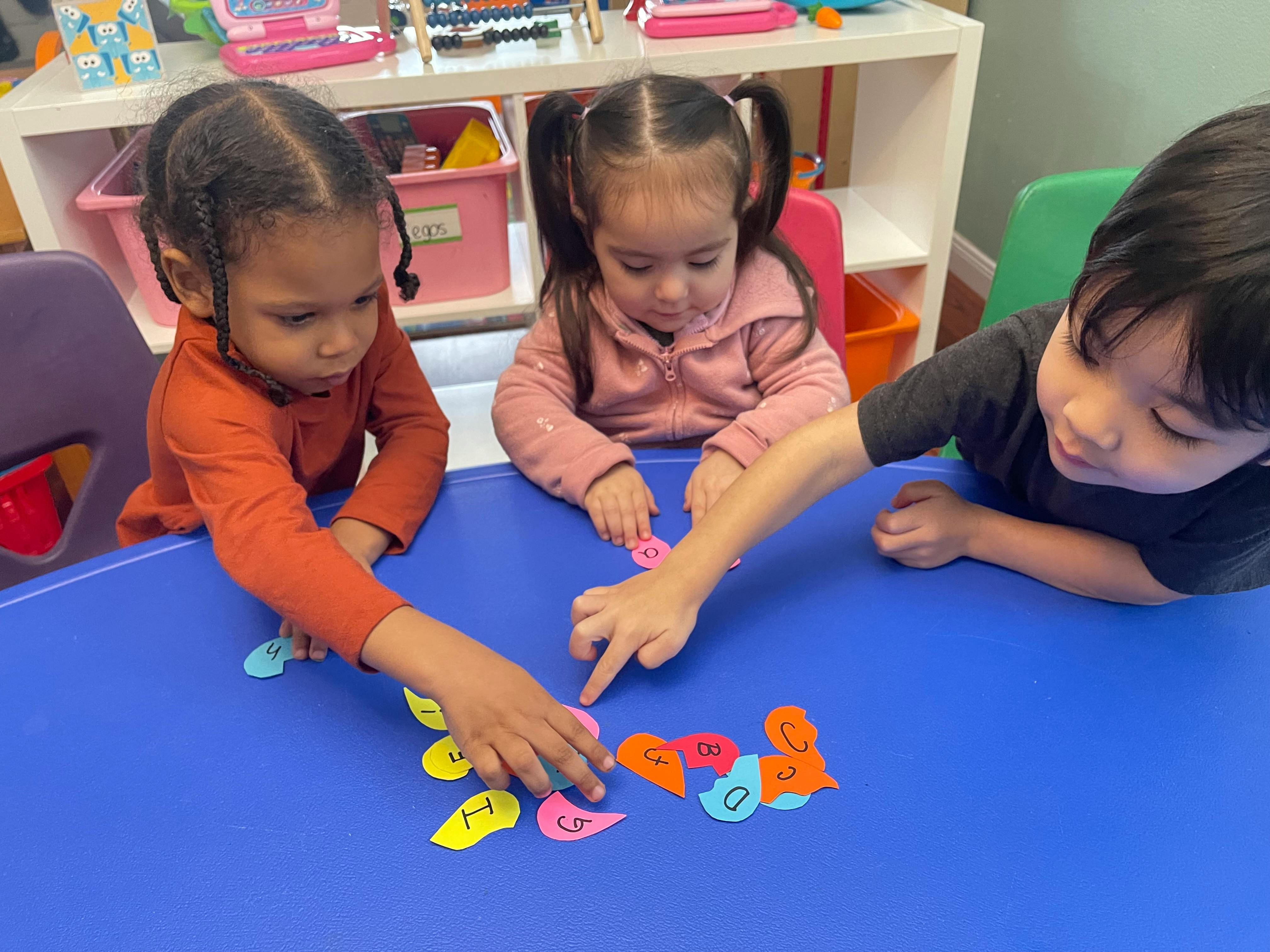 Three children playing with colorful cutouts on a blue table