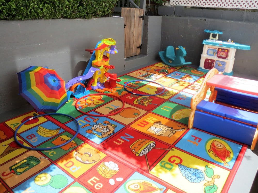 Colorful playmat with various toys including a slide, umbrella, and hula hoops