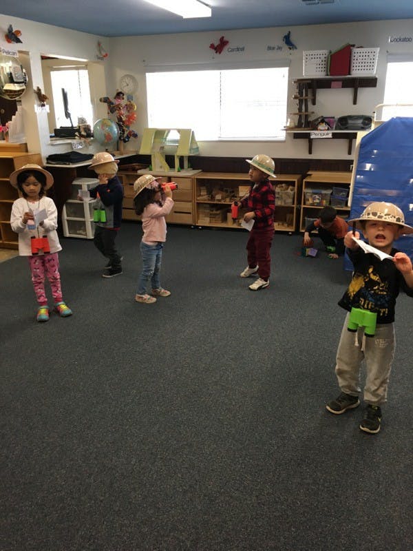 Children in safari hats playing with toy binoculars in a classroom