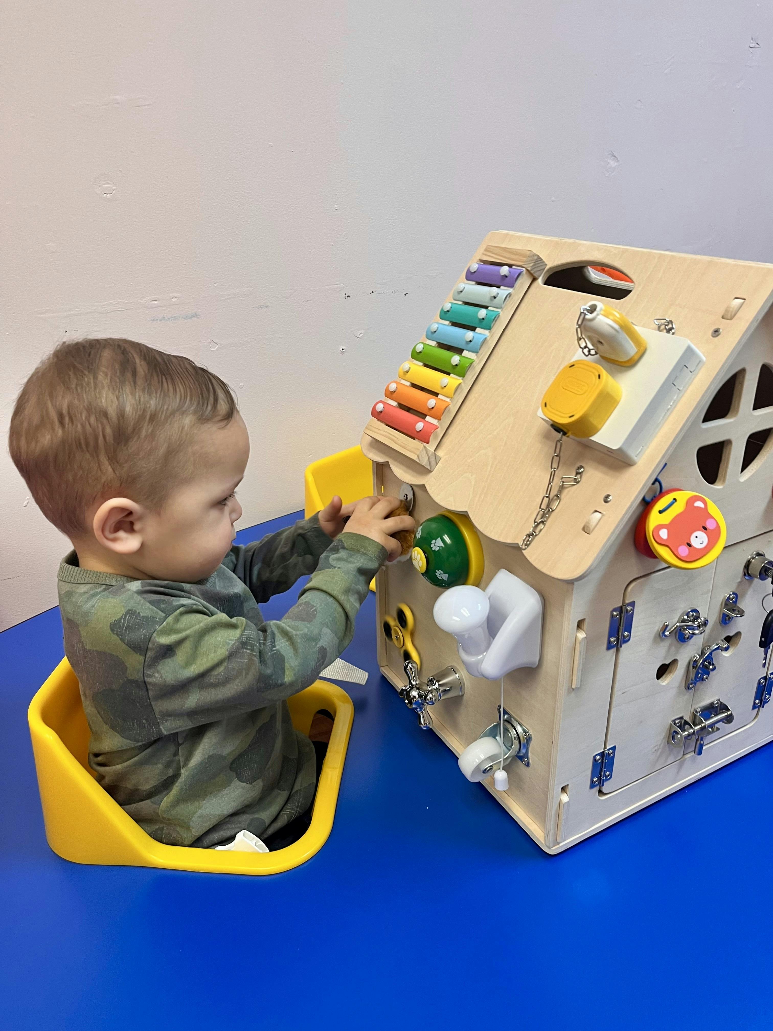 Child playing with a busy board house on a blue table