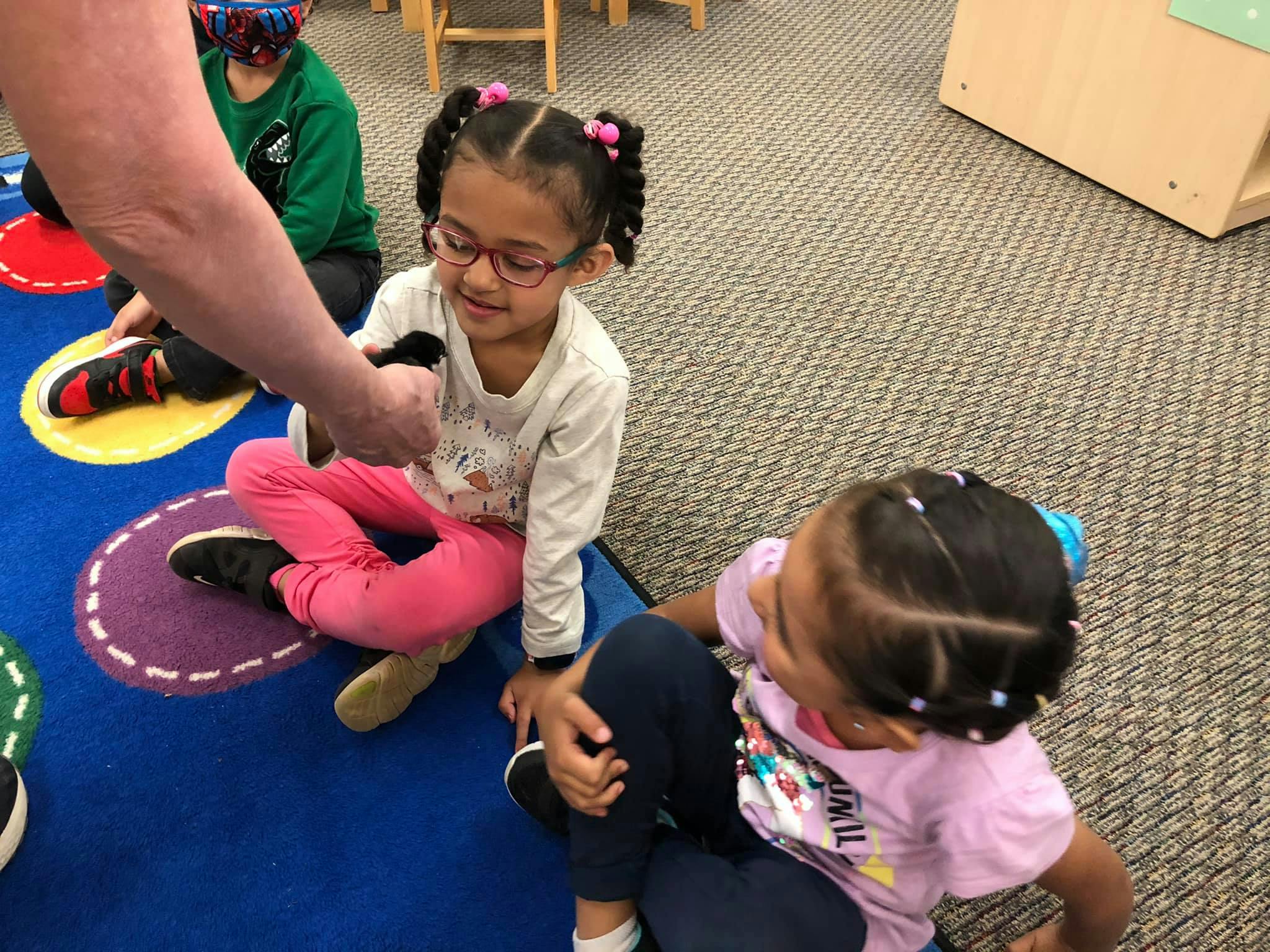 Adult handing an object to a child sitting on a blue rug