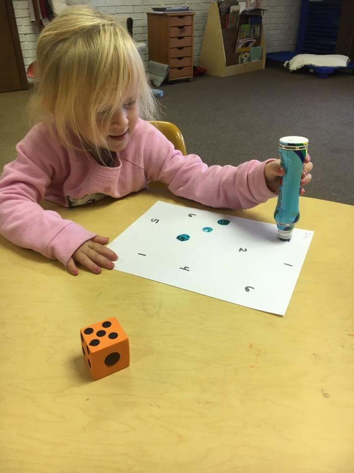 Child using a paint dauber on a paper with numbers and an orange die