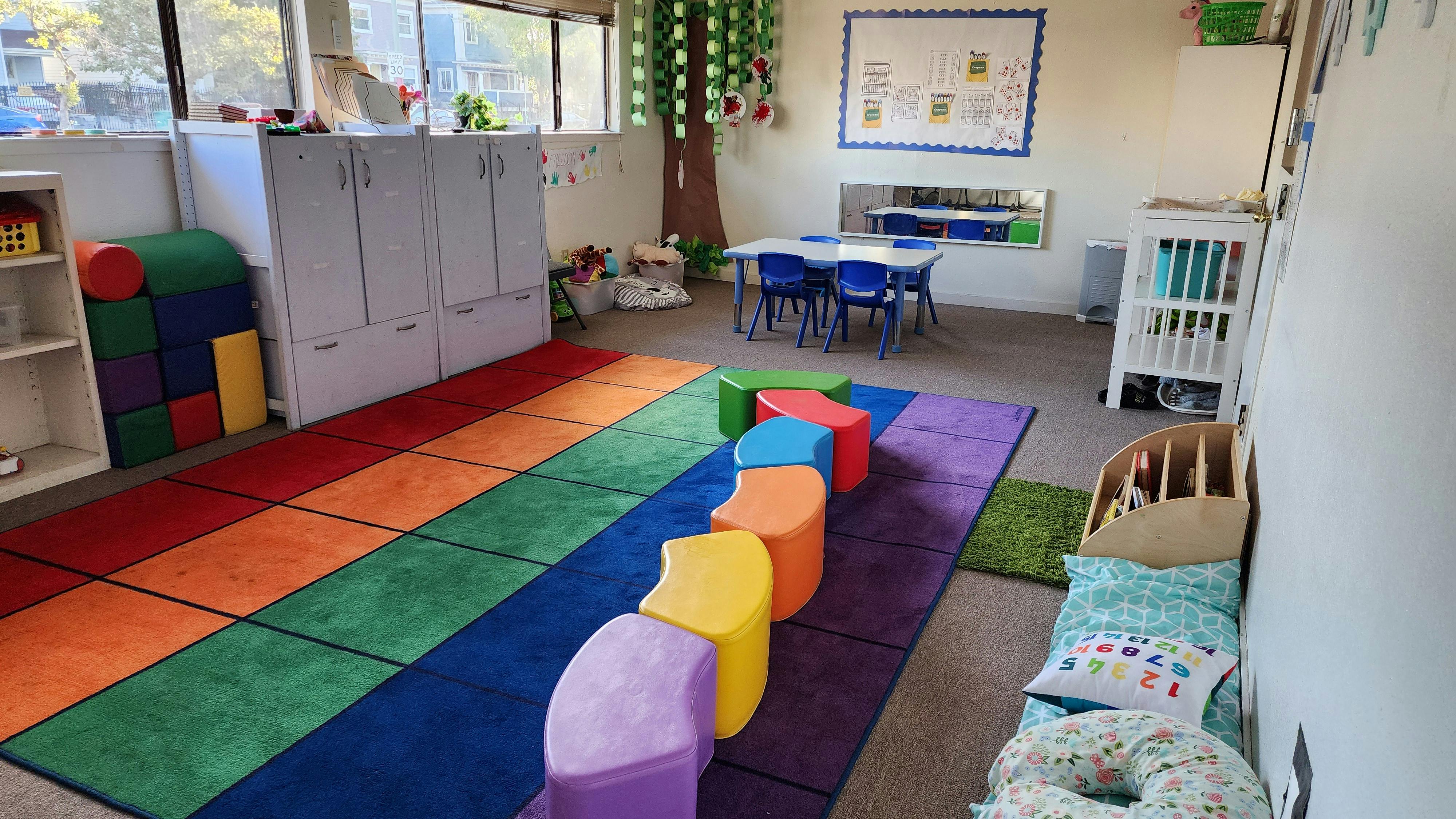Colorful classroom with toy storage, small chairs, and a rainbow floor rug