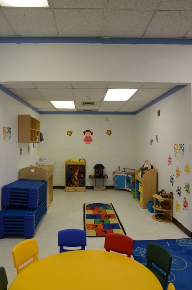 Empty classroom with small tables and chairs, play kitchen, and colorful rug