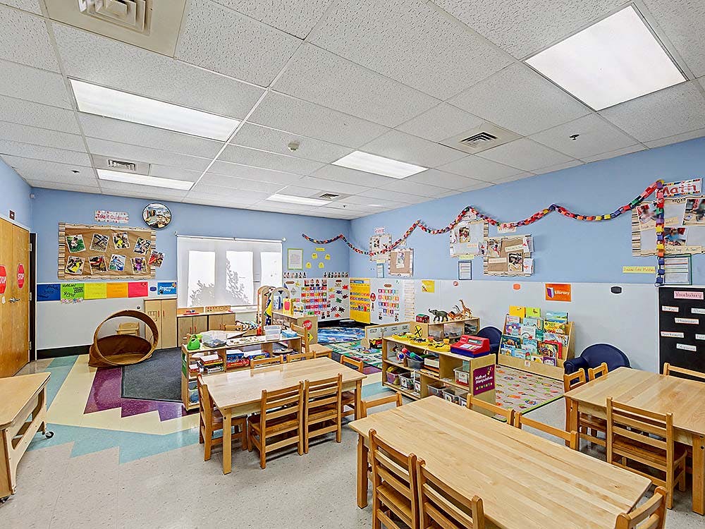 Classroom with small wooden tables and chairs, toys, and educational posters