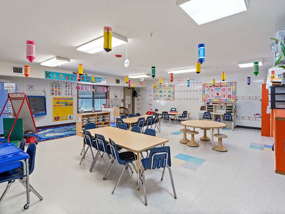 Classroom with tables and chairs, decorated with posters and hanging crayon cutouts