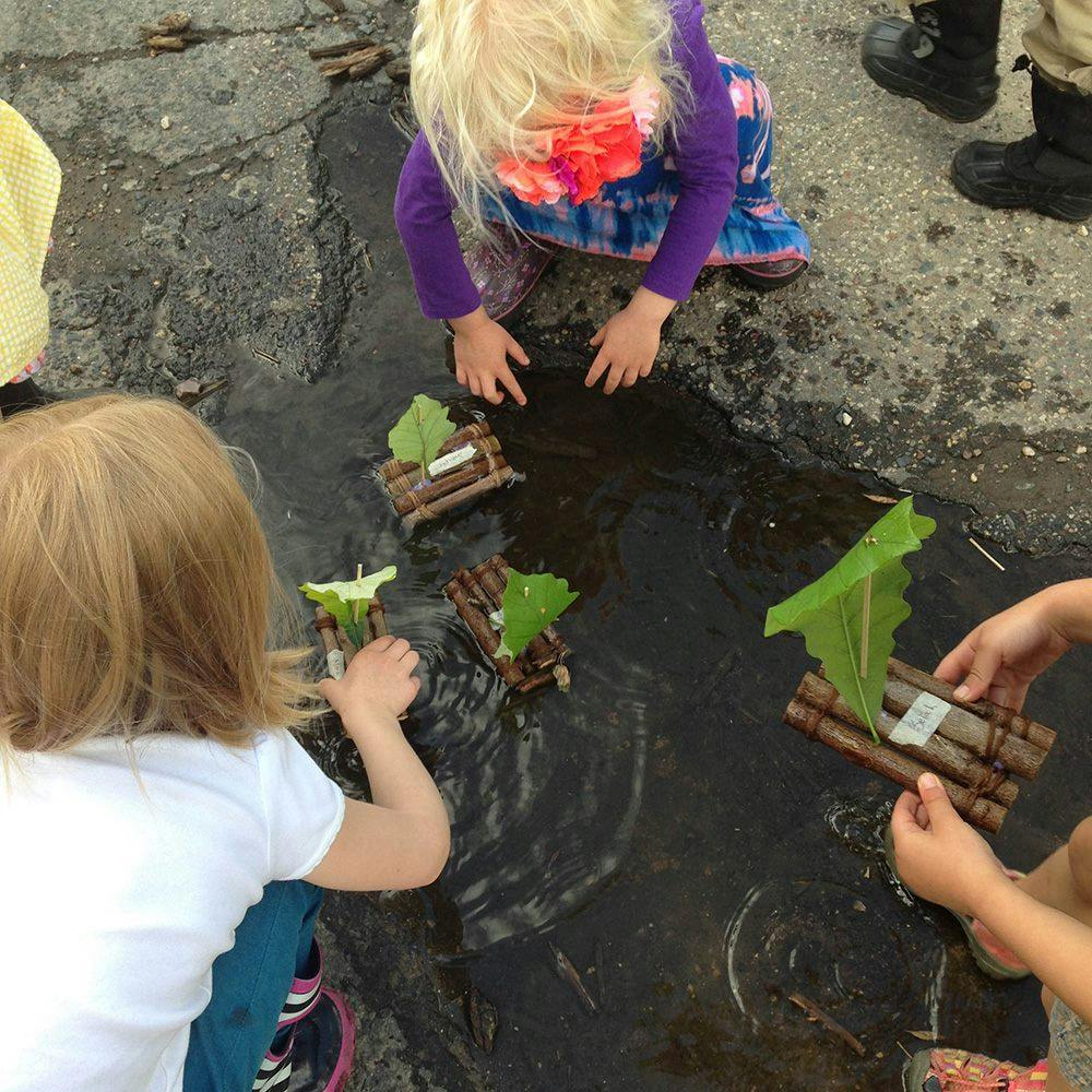 Children playing with toy boats in a puddle