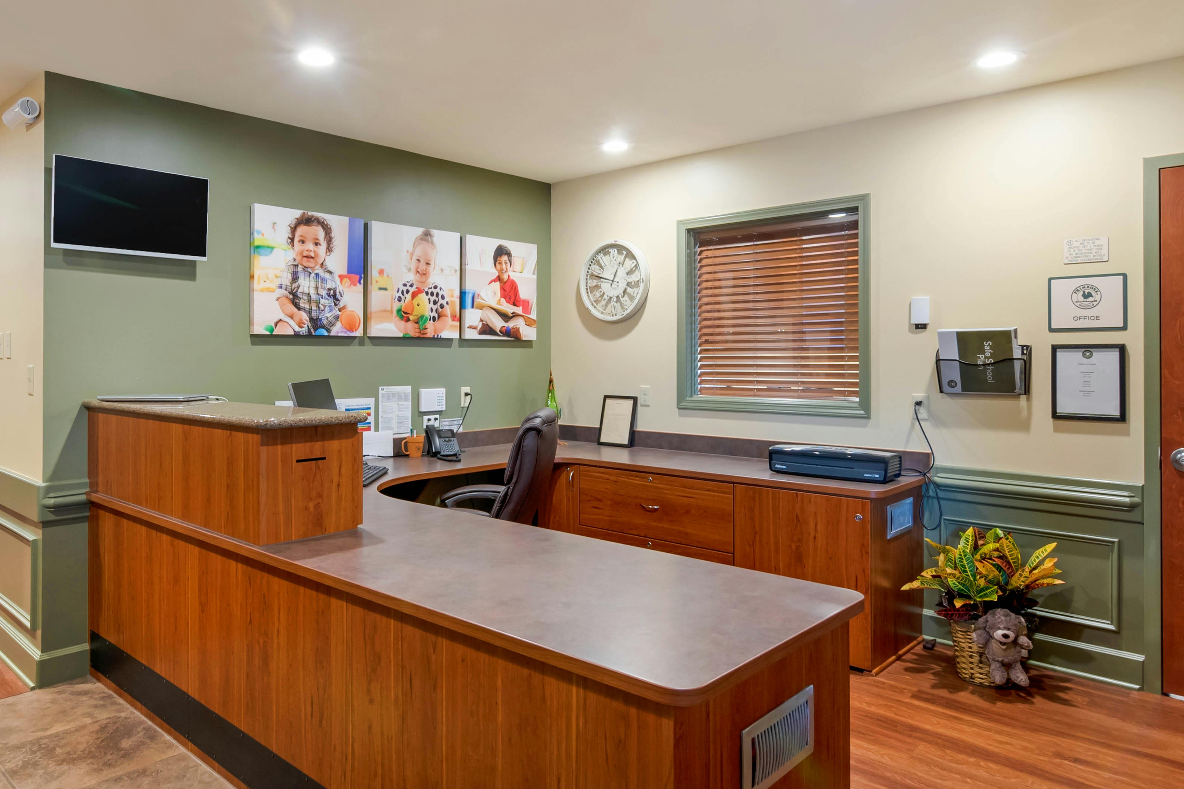 An empty reception desk with office equipment and three photos of children on the wall