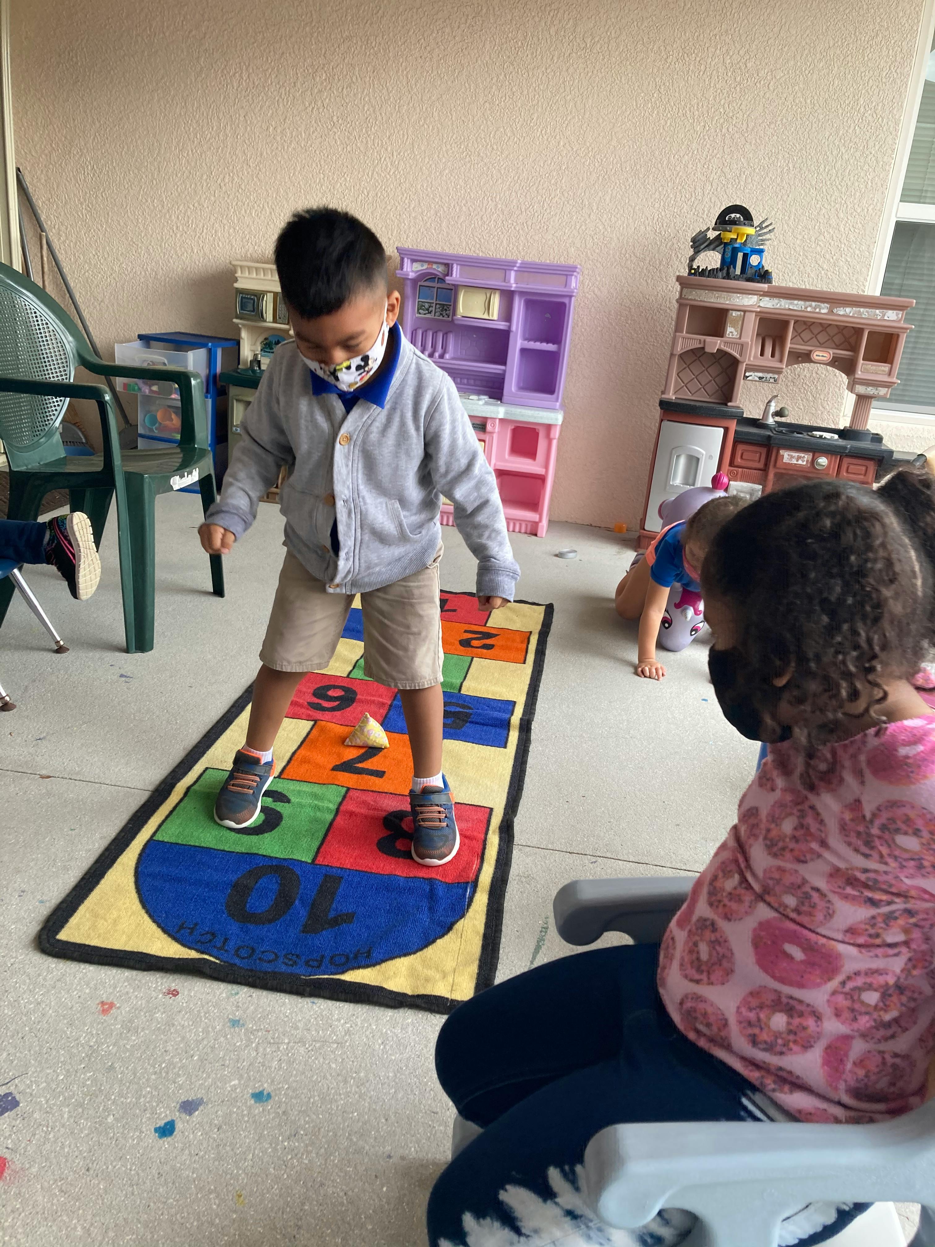 Child in a mask playing hopscotch on a colorful mat
