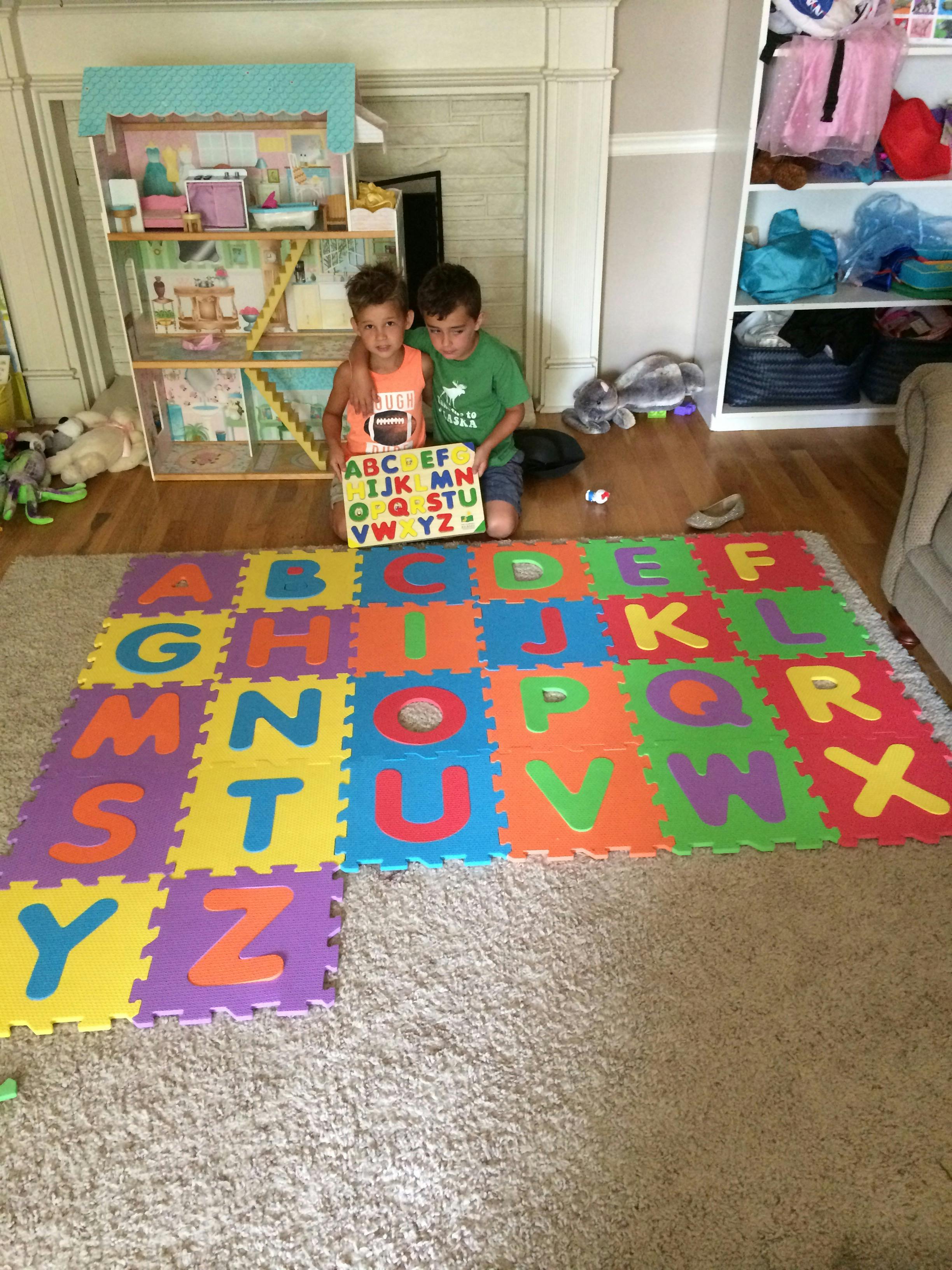 Two children holding an alphabet board next to alphabet floor mats