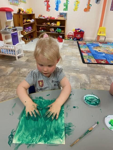 Child finger painting with green paint on paper