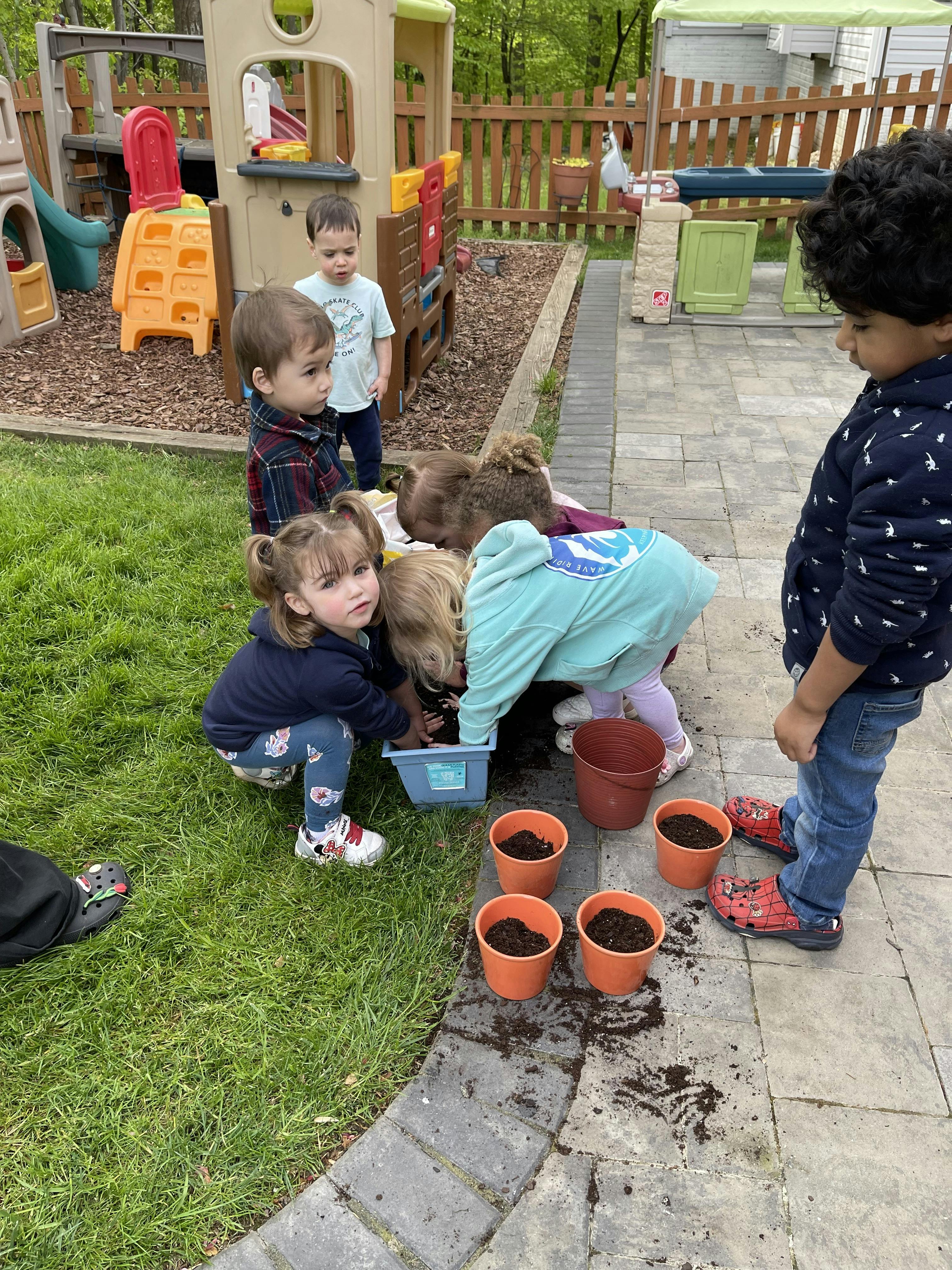 Group of children playing with soil and planting pots in a backyard