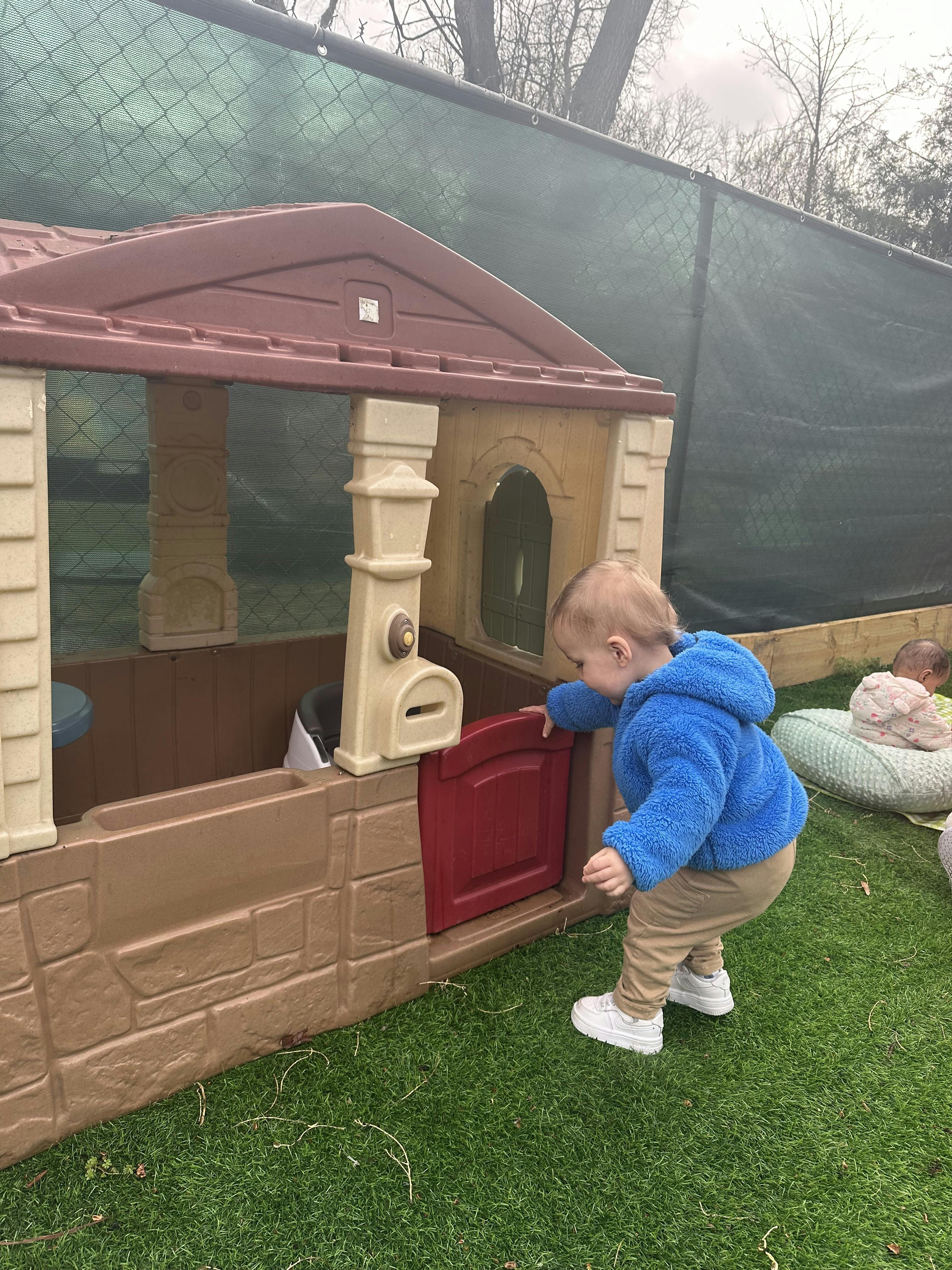 Child in blue jacket playing at a brown playhouse