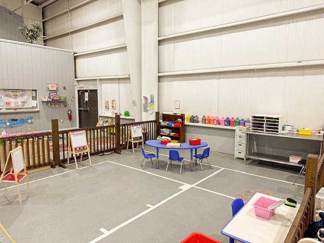 Childcare activity room with small tables, chairs, and easels