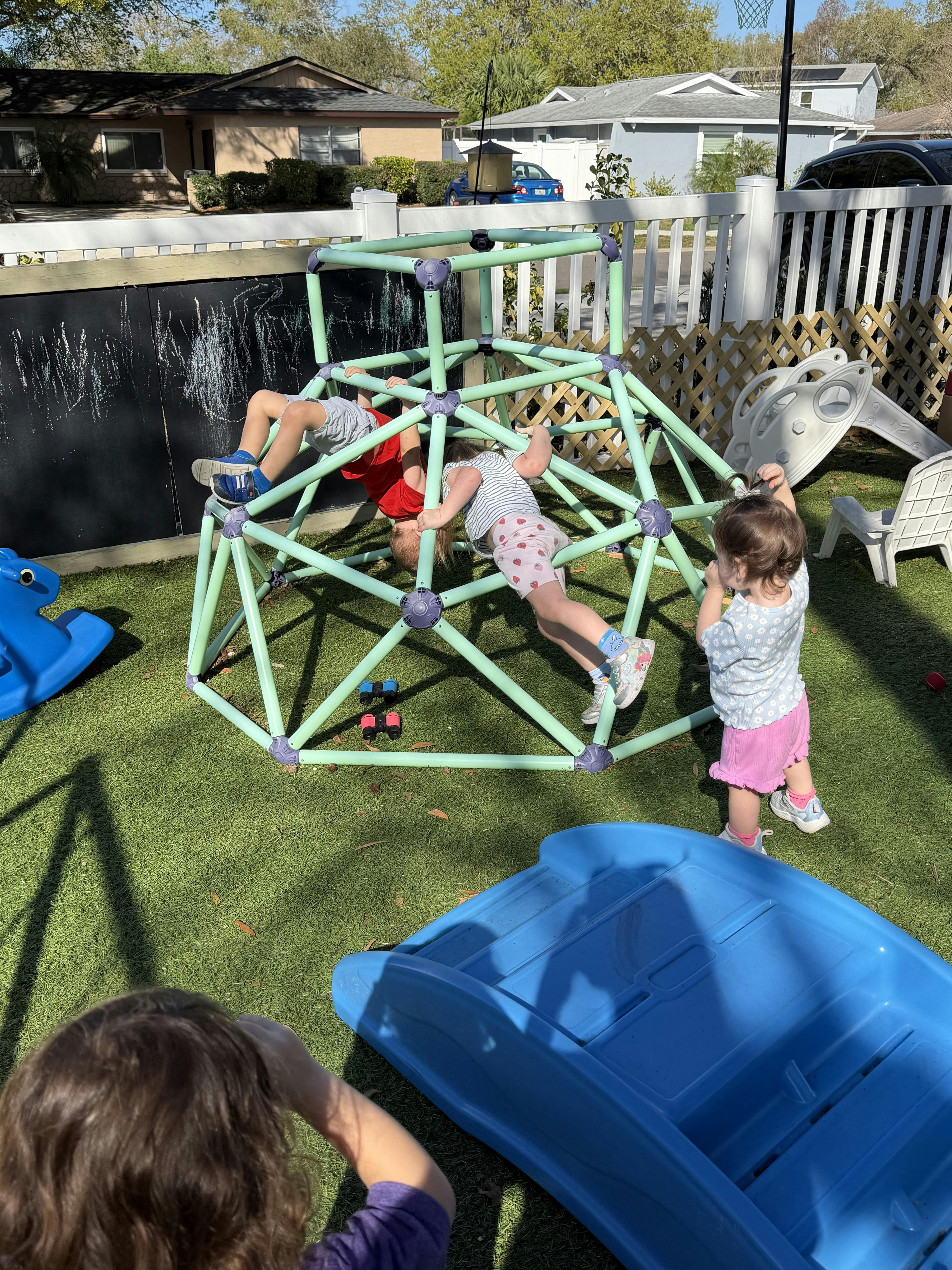 Three children playing on a green geodesic dome climber on artificial turf
