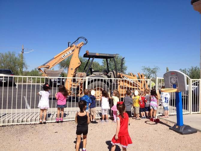 Children looking through a fence at a backhoe