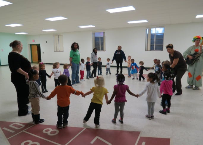 Adults and children holding hands in a circle in a large room
