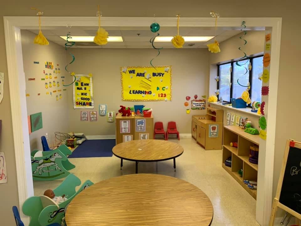 Classroom with round tables and yellow signs on the wall that says "We are busy learning"