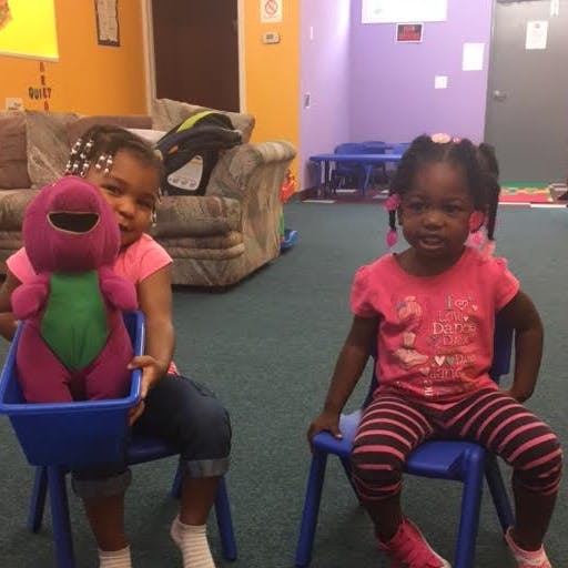 Two children sitting on chairs, one holding a purple stuffed animal