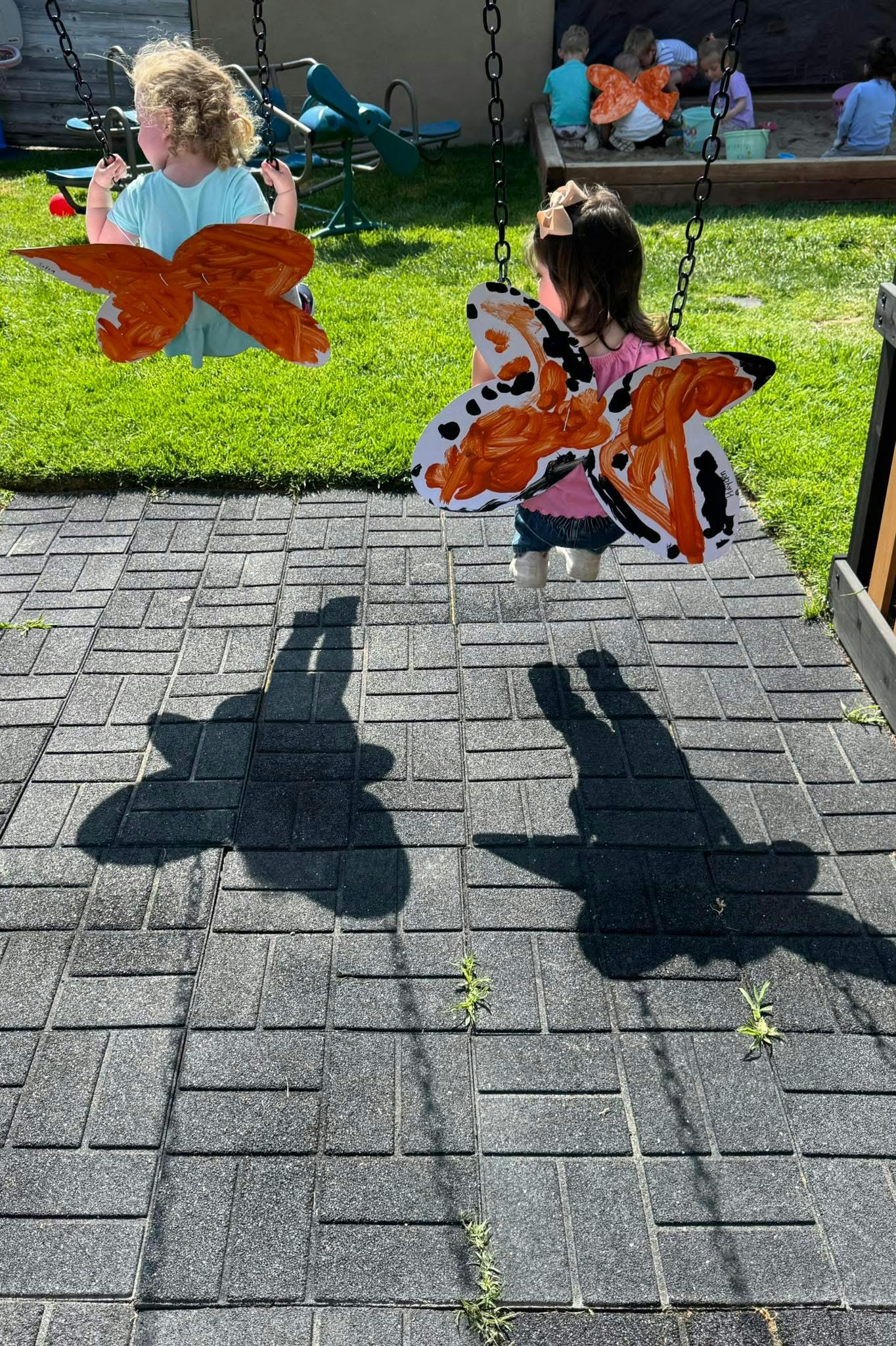 Two children on swings with butterfly wings attached to the front