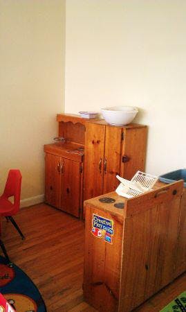 Wooden play kitchen set with a red chair and rug